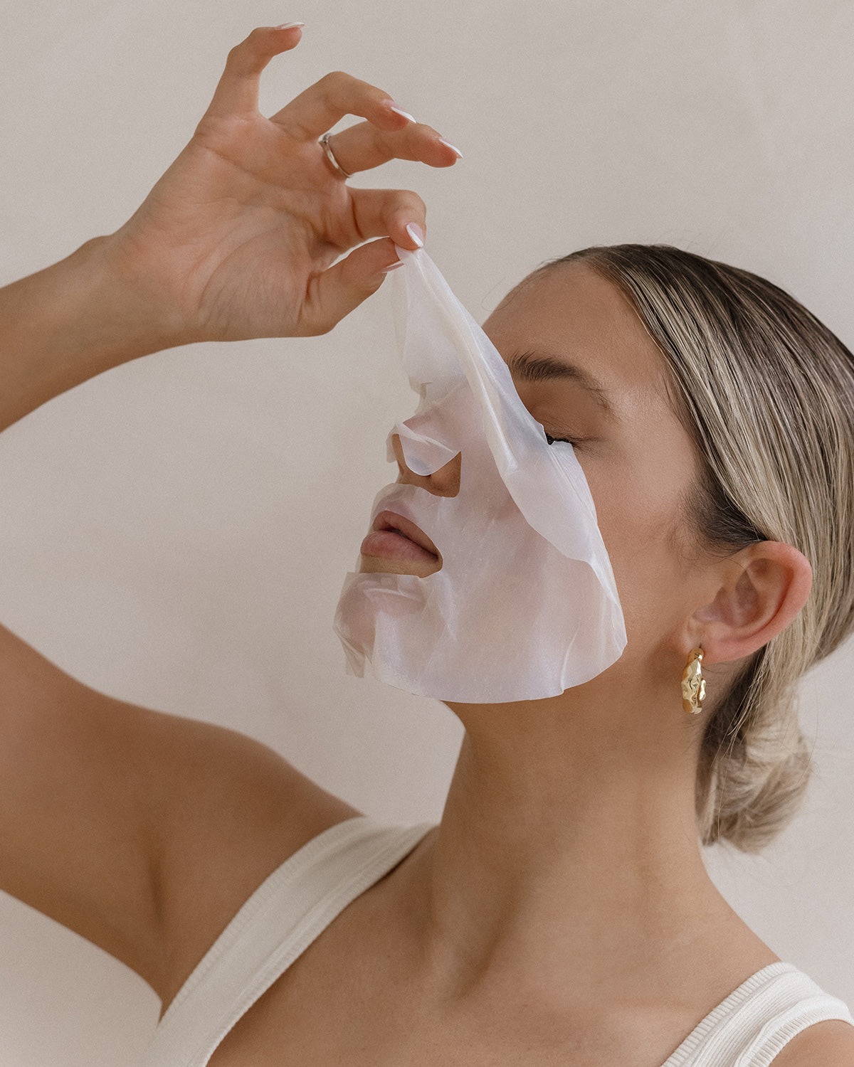 Person applying a ProPlenish face mask to their face with a neutral background