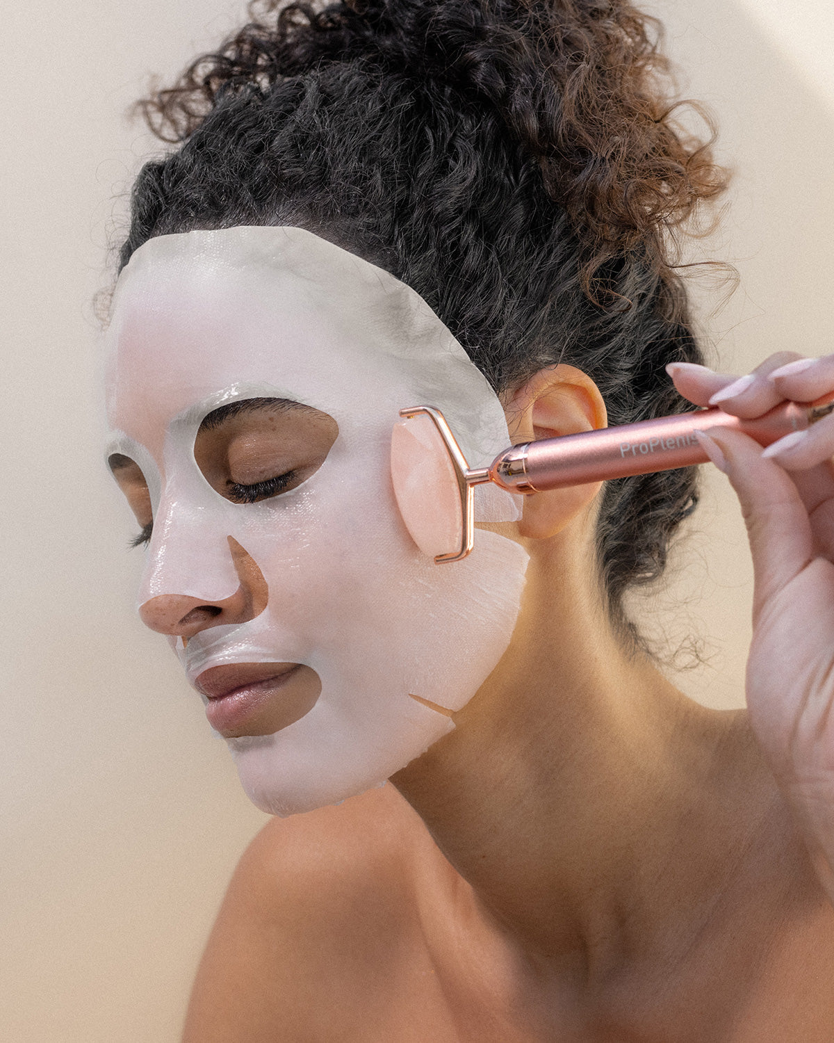 Person applying a face mask with a rose quartz roller tool against a neutral background